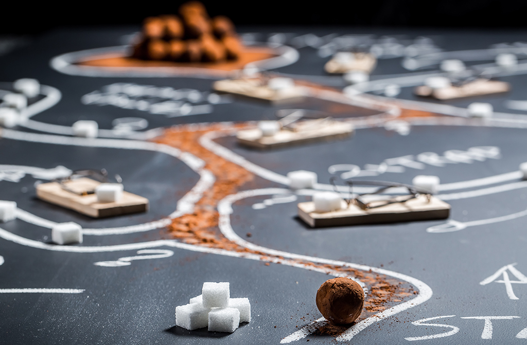 Matte mit aufgemahltem Labyrinth, durch das eine Schokoladen Kugel mit Strategie den richtigen Weg entlang rollt.