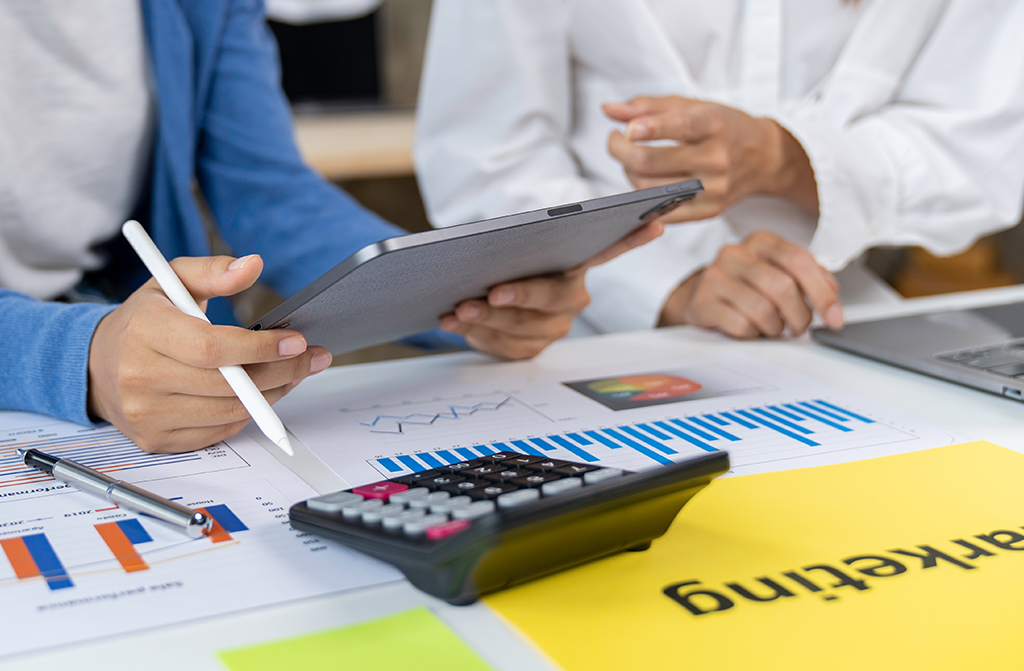 Zwei Personen sitzen an einem Tisch. Eine Person wird beraten, indem ihr etwas auf einem iPad gezeigt wird.