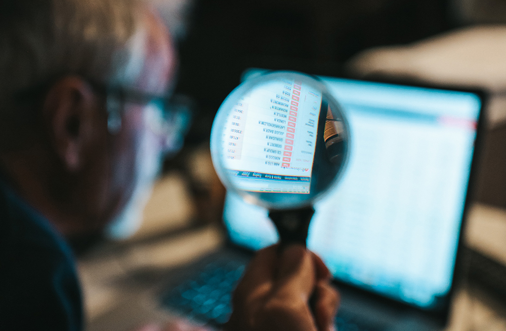 Mann analysiert mit einer Lupe Marketing Nummern auf einem Laptop Screen