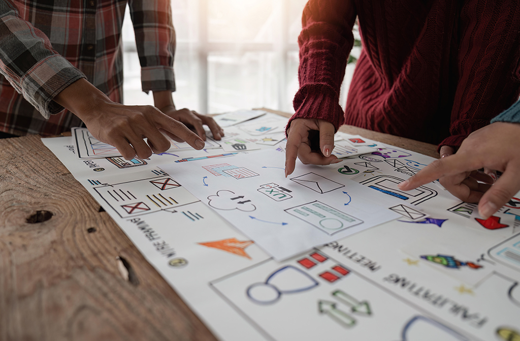 Personen deuten auf ein großes Blatt Papier mit Marketing Umsetzungsideen