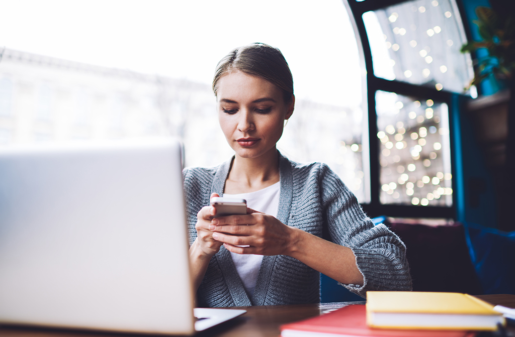 Frau vor einem Laptop schaut auf ihr Handy